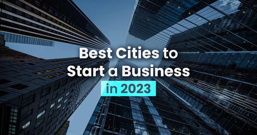 Text overlay 'best cities to start a business in 2023' on an upward view of modern skyscrapers under a blue sky.